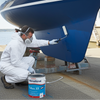Person painting a large blue boat with a can of International Paints Tiflux 33 on a dock.