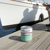 Man working on a sailboat with a can of International Primocon paint on a dock.