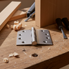 Woodworking scene with metal hinge, screws, and tools on a wooden surface.