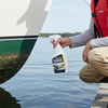 Man cleaning a boat with a cleaning product on a dock by a lake.