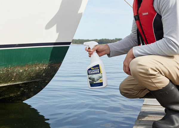 Man cleaning a boat with a cleaning product on a dock by a lake.