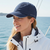 Woman wearing a navy cap and white jacket on a boat with ocean in the background