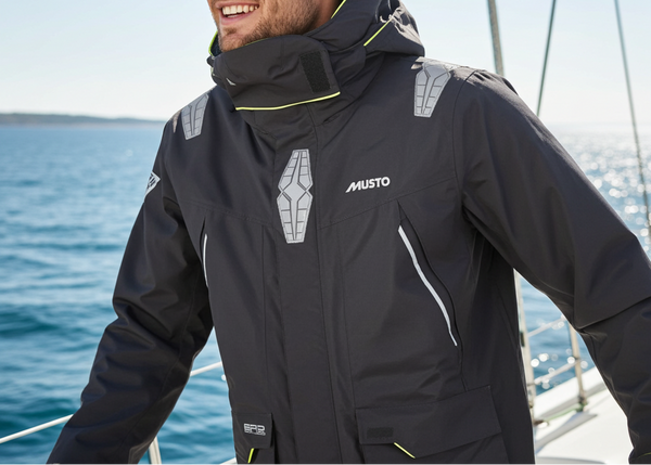 Man wearing a black Musto jacket on a boat with blue water and clear sky in the background