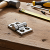 Metal hinge on a wooden surface with tools including a hammer, screwdrivers, and a ruler.