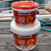 Two containers of Norski epoxy glue on a wooden dock with water and a boat in the background.