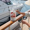 Person holding a bottle of teak oil on a boat docked at a marina