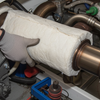 Person wearing gloves handling a cylindrical object with insulation in an industrial setting