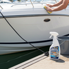 Man cleaning a boat with a bottle of cleaning solution on a dock.