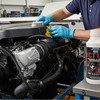 Man working on a vehicle engine with a bottle of engine cleaner in a workshop.