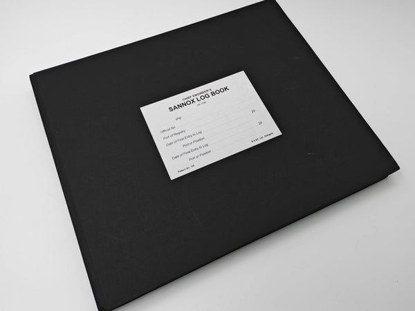 A black hardcover notebook or log book with a white paper label reading 'SANNOX LOG BOOK' on a plain white surface.