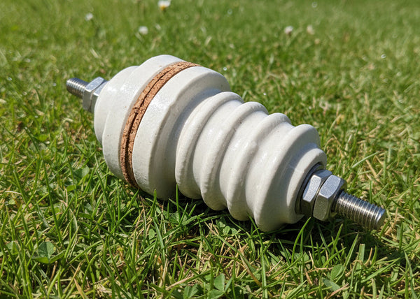 A ceramic high-voltage spark plug insulator with a ribbed white body, a brown insulating band, and silver metal threaded ends, shown on a plain white background.