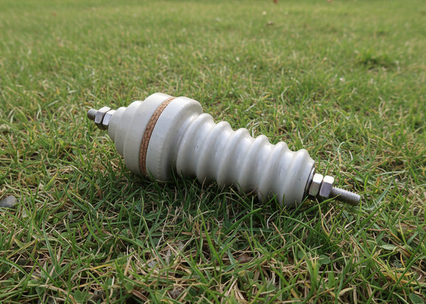 An industrial ceramic high-voltage insulator with a ribbed body, a brown insulating band, and metal terminal nuts on both ends, shown on a plain white background.