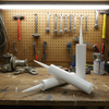 Three white plastic caulking or adhesive squeeze tubes with pointed applicator nozzles, arranged on a clean light gray studio background.