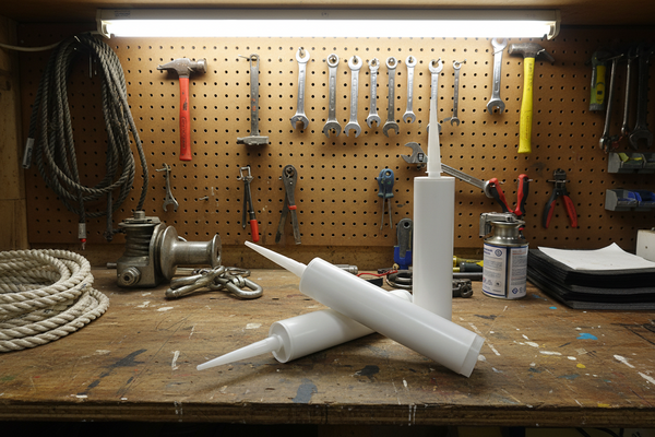 Three white plastic caulking or adhesive squeeze tubes with pointed applicator nozzles, arranged on a clean light gray studio background.