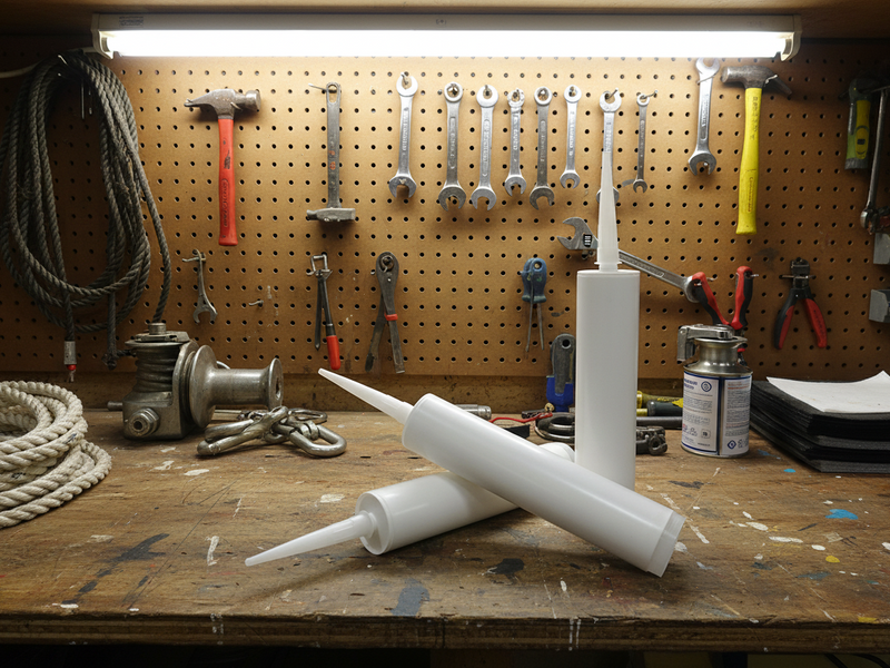 Three white plastic caulking or adhesive squeeze tubes with pointed applicator nozzles, arranged on a clean light gray studio background.