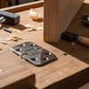 Metal hinge on a wooden workbench with tools and wood shavings.