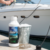 Person cleaning a boat with a bottle of cleaner and a bucket on a dock.