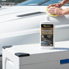 Person polishing a boat with a bottle of marine polish in the foreground.