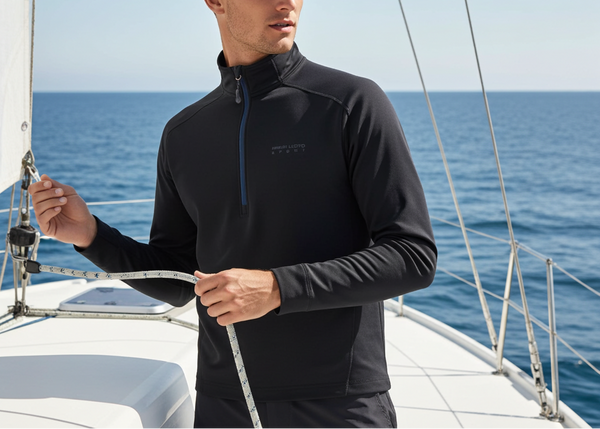 Man wearing a black jacket on a sailboat with blue ocean and sky in the background