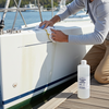 Man cleaning a sailboat with a bottle of cleaning solution on a dock.
