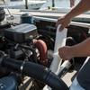 Person working on a boat engine at a dock with other boats in the background.