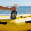Person holding a bottle of vinyl guard on a yellow inflatable raft by the ocean.