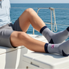 Man sitting on a boat wearing gray socks with a blue sea and sky background