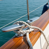 Close-up of a boat's railing with a rope and cleat, set against a backdrop of water and sky.