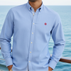 Man wearing a light blue shirt with a red logo on a boat with ocean view