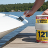 Person holding a paintbrush near a container of ADOS 121 repair paint on a dock by a lake.