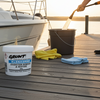 Person cleaning a boat with a bucket and cleaning supplies on a dock at sunset.