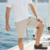 Man in white polo shirt and beige shorts on a sailboat with water and sky in the background