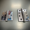 Two metallic hinges on a reflective surface